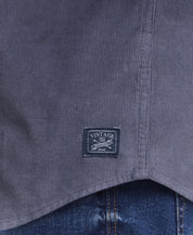 Close-up of THIN WALE SOLID CORD SHIRT tag showcasing vintage logo on textured fabric in poppy seed color.