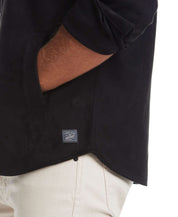 Detail of unlined sueded shirt jacket in black, showcasing soft fabric and side pocket with label.
