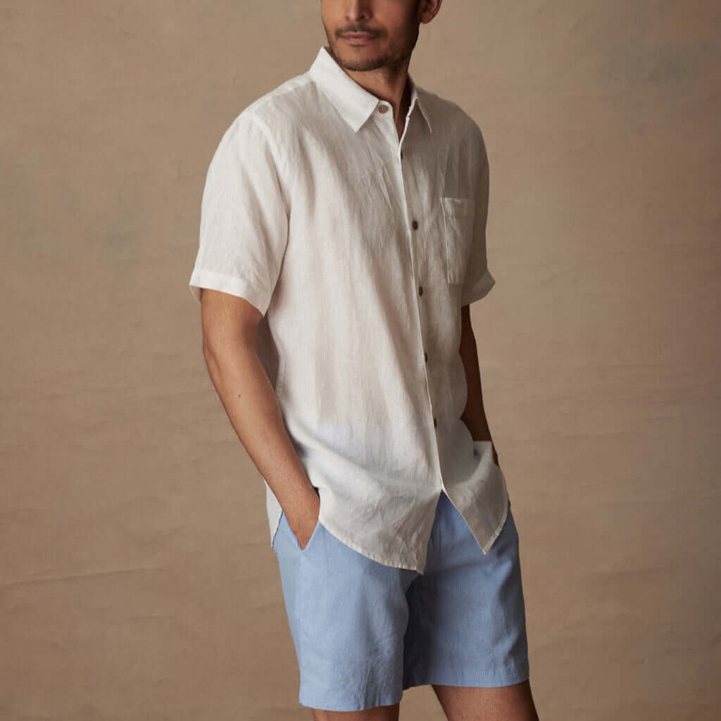 Model wearing a classic short sleeve white linen shirt, featuring a button closure and front pocket.