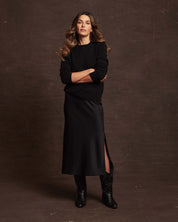 Woman wearing a black 100% cashmere long sleeve crew sweater paired with a sleek black skirt.
