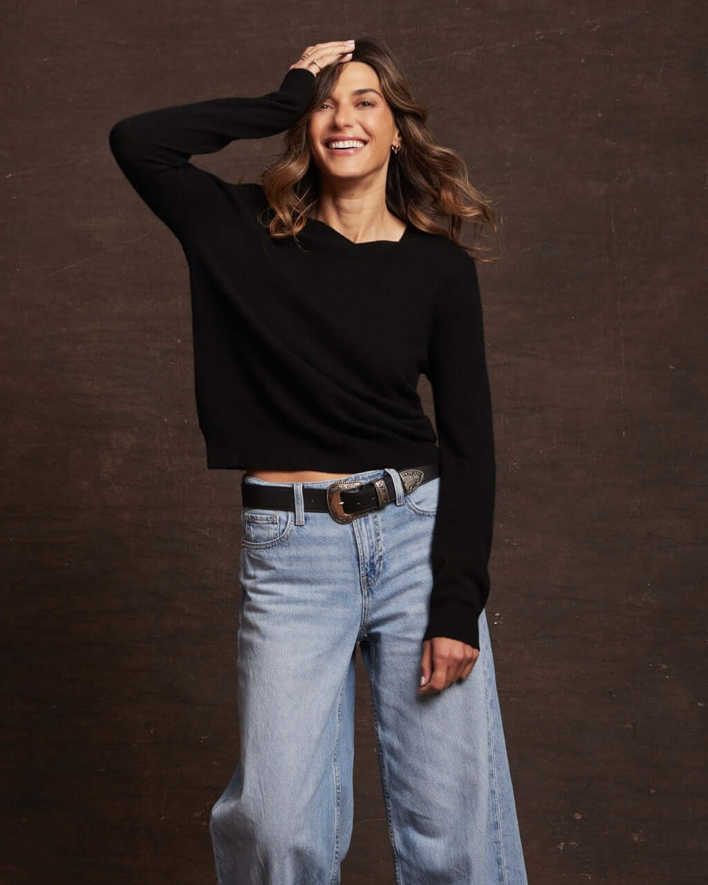 Smiling woman wears a women's black cashmere long sleeve sweater with V-neckline and relaxed fit, styled with jeans.