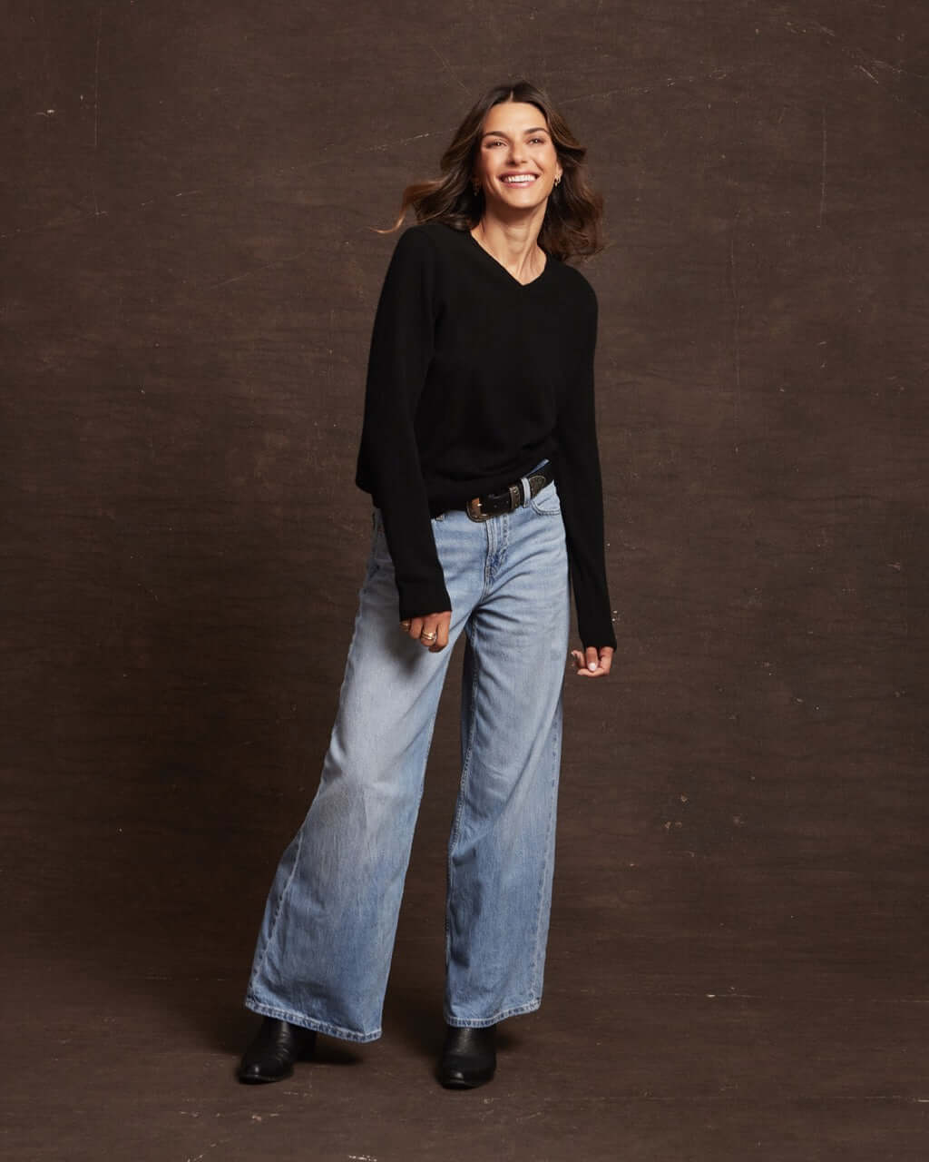 Model wearing a women's black cashmere long sleeve V-neck sweater paired with wide-leg jeans.