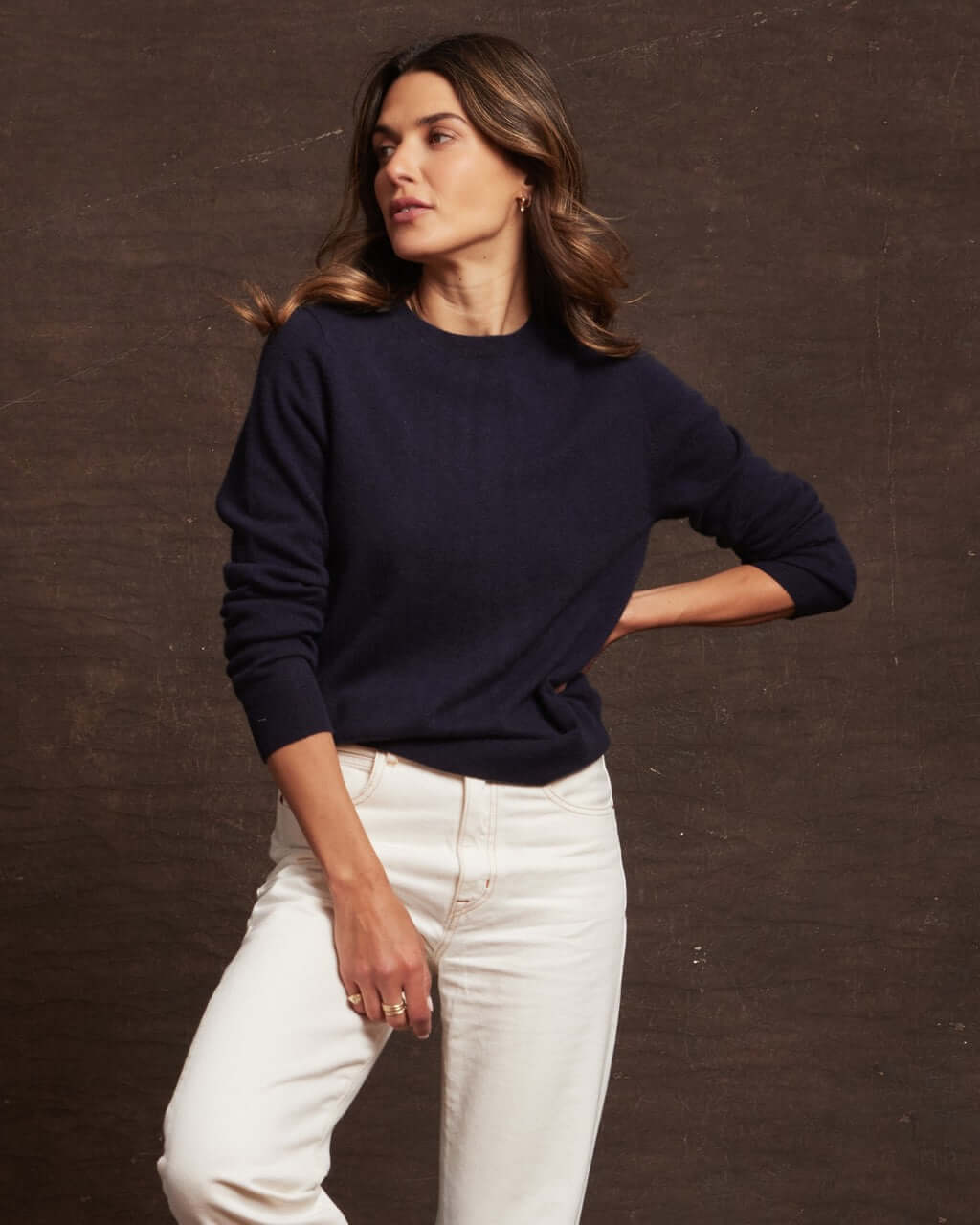 Model wearing a women's dark navy cashmere long sleeve crew sweater, styled with white jeans.