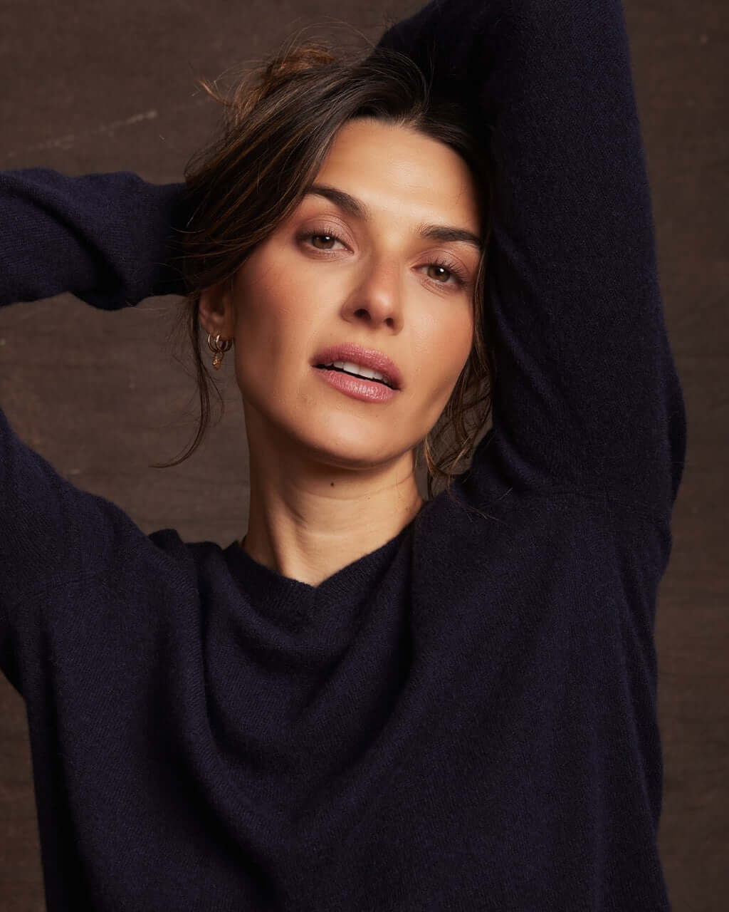 Woman showcasing a women's 100% cashmere long sleeve solid V-neck sweater in dark navy against a textured background.