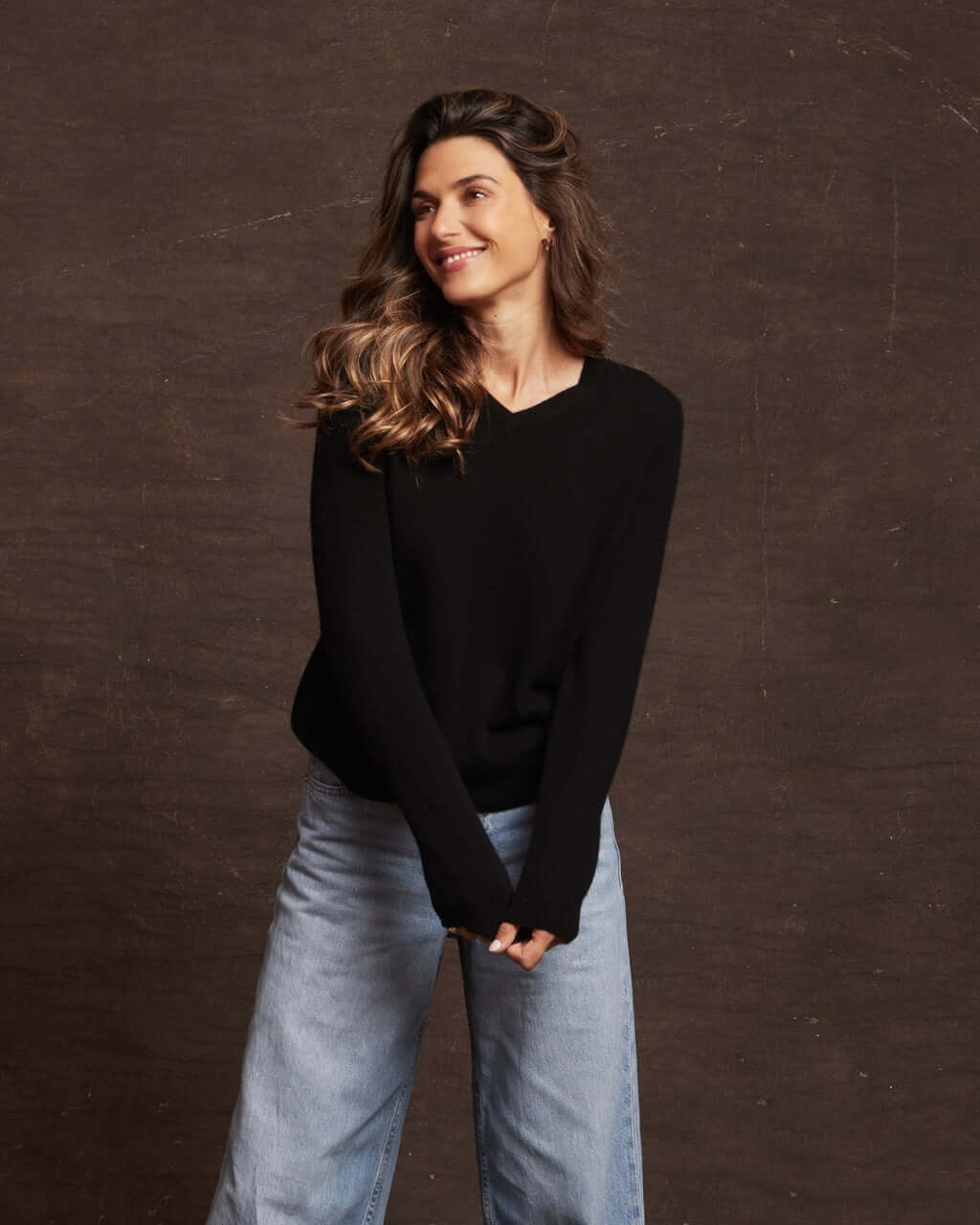 Woman wearing a black long sleeve cashmere sweater with a V-neckline and relaxed fit, styled with jeans.