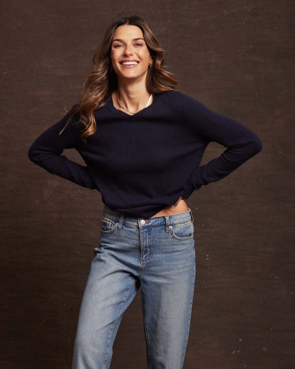 Woman smiling in a dark navy cashmere long sleeve sweater paired with jeans, showcasing comfort and style.