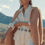 Woman wearing a women's plush coatigan in apricot over a textured white shirt, styled with a fashionable belt in an outdoor setting.