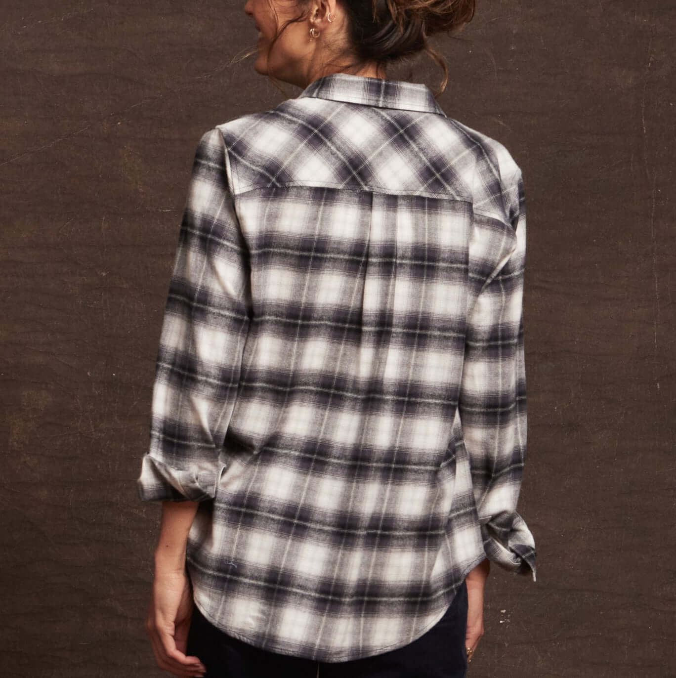 Back view of a woman wearing a black and white plaid women's stretch flannel shirt, showcasing its classic fit and rolled sleeves.